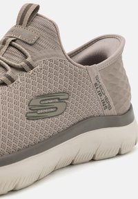Beige, mesh material slip-on sneaker with a textured design. Features a gray outsole and subtle branding on the side. Light cushioning visible.