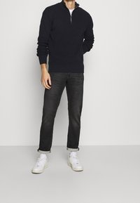 Pull marin en tricot bleu marine avec une demi-fermeture éclair, poignets et ourlet côtelés, assorti à un jean foncé retroussé et des baskets blanches.