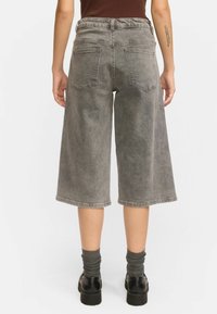 Culottes en denim gris avec une coupe loose, longueur mi-mollet, taille élastique et deux poches arrière. Tissu texturé avec une finition délavée.