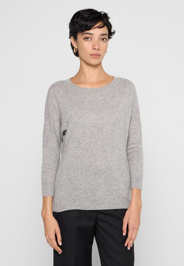 Lichtgrijze trui van zachte stof, met een ronde hals, driekwart mouwen en een relaxed fit. Draagt met donkere broeken.
