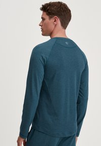 Langarm teal sportshirt met een ronde hals en vlakke naden, voorzien van een logo op de bovenrug, gemaakt van een zachte, gestructureerde stof.