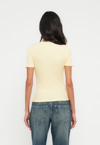 T-shirt ajusté jaune clair, manches courtes, texture côtelée, assorti à un jean denim bleu taille mi-haute, avec poches standard et effet délavé.