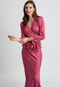 Czerwona sukienka o kroju wrap z długimi rękawami, dekoltem w kształcie litery V oraz peplum w talii. Gładka tekstura i dopasowany krój.