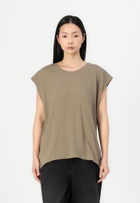 T-shirt de culoare verde măsliniu, cu mâneci scurte, realizat dintr-un material moale, având un decolteu rotund și o croială relaxată, lejeră. Modelul poartă pantaloni negri.