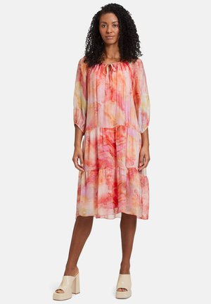 Fließendes, gestuftes Kleid in rosa und orangefarbenen Aquarellmustern. Mit gepufften Ärmeln und einem Bindekragen. Kombiniert mit beigen Plateauschuhen.