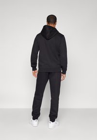 Svart hettegenser med matchende joggebukser, med en avslappet passform og ribbede mansjetter. Brukt sammen med hvite joggesko. Enkelt design.