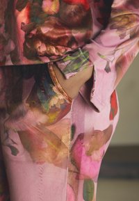 Kwiatowy komplet piżamowy w odcieniach różu i zieleni, wykonany z jedwabistej tkaniny, o luźnym kroju, z boczną kieszenią i subtelnym metalicznym akcentem na krawędziach.