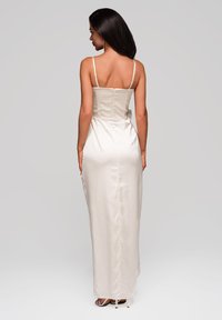 Lungo vestito in raso di colore avorio con spalline sottili, un corpetto aderente e una gonna liscia che arriva a terra, caratterizzata da una sottile texture.