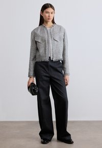 Γκρι κροπ μπουφάν από τουίντ με ξεφτισμένα άκρα και δύο μπροστινές τσέπες, συνδυασμένο με μαύρο παντελόνι φαρδιάς γραμμής και μαύρη τσάντα χειρός.