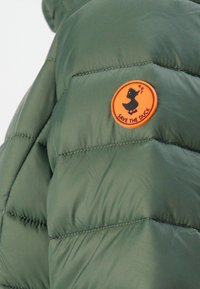 Groen gewatteerd jack met een ronde oranje patch waarop een zwarte eendensilhouet en de tekst "BESCHERM DE EEND" op de schouder staat.