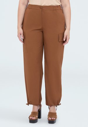 Pantalon cargo marron avec bouton et taille élastique, poches latérales à rabat, cordons ajustables aux chevilles, porté avec des sandales à plateforme marron.