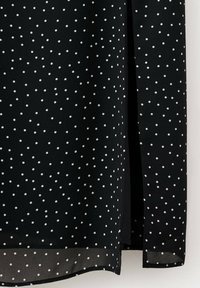 Tissu noir à petits pois blancs avec une fente latérale près de l'ourlet.