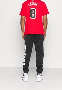 Camiseta roja con "LAVINE" y el número "8" en negro en la parte posterior; combinada con pantalones jogger negros que tienen texto blanco y puños elásticos, usados con zapatillas blancas.