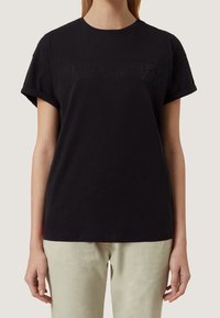 Černé bavlněné tričko s ohrnutými rukávy a rovný střihem, s tónovým nápisem z kamínků přes hrudník.