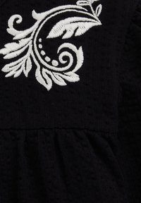 Must mustriga kangas sisaldab valgeid tikandeid lehe- ja keerisekujundite kujul. Alumises osas on kogumiskaunistus, mis parandab kogu välimust.