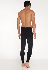 Leggings noirs avec une coupe près du corps, texture lisse et une taille arborant un petit logo. Conçus pour un usage sportif ou décontracté.