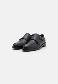 Black leather shoes with a rounded toe, single strap across the instep, and metal buckle detail. Smooth texture and low-profile design.