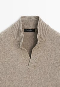 Light beige knit sweater with ribbed half collar and V-neck opening, featuring a black label with white "Massimo Dutti" text inside the collar.