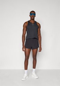 Débardeur de sport noir avec un détail réfléchissant, associé à un short noir assorti. Porte des chaussettes blanches et des baskets blanches imposantes.