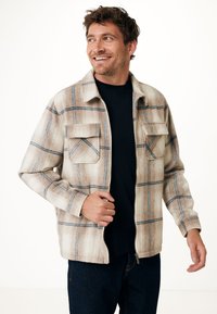 Plaid jacket featuring a cream, beige, and blue color scheme. Made of a soft, textured fabric, it has a front zipper and two chest pockets.