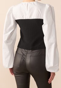 Bodice noir en maille côtelée se transforme en manches bouffantes blanches, associé à un pantalon taille haute en simili cuir, avec des poches arrière et une texture lisse.
