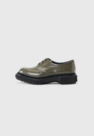 Olive green glossy lace-up shoe with thick, chunky black ridged sole, low heel, and smooth rounded toe on a plain background.