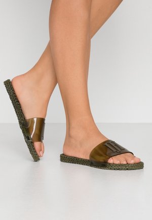 Des sandales à glissière vert olive avec une bride brillante et une semelle tissée. La bride présente une finition texturée et un accent logo audacieux.