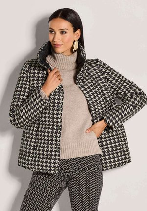Gestepte jas in een houndstooth patroon met zwarte en crème kleuren. Voorzien van een hoge kraag en knopen, gecombineerd met een beige trui.