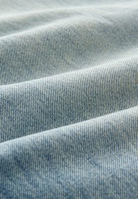 Heled sinine denimkangas, millel on peened vertikaalsed triibud ja veidi tekstureeritud pind, näidates pehmeid voldikuid ja siledat viimistlust.