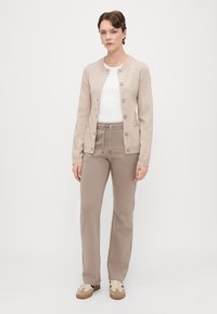Cardigan bej cu guler rotund, deschidere cu nasturi, manșete ribbate, asociat cu pantaloni de trening bej și adidași bej. Textură netedă, design casual.