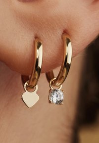 Golden hoop earrings featuring a heart charm and a clear crystal pendant, highlighting smooth surfaces and shiny finishes.