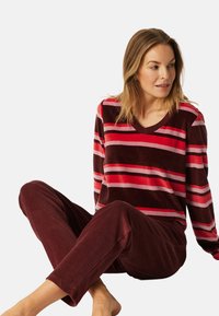 Conjunto de loungewear de terciopelo marrón con rayas horizontales rosas y rojas; parte superior de manga larga con escote en V y pantalones ajustados a juego.