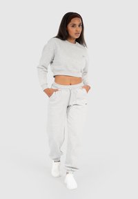 Felpa grigia corta e pantaloni jogger coordinati realizzati in tessuto morbido. Entrambi presentano una vestibilità comoda, polsini elastici e tasche laterali.