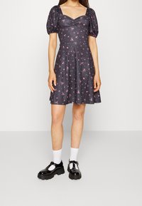 Tmavé květinové šaty s nap puff rukávy, čtvercovým výstřihem a dobře padnoucím tělem. Černé chunky boty s bílými ponožkami. Vzor obsahuje malé růžové květiny.