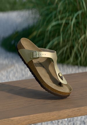 Gold thong sandal with a smooth synthetic upper, adjustable buckle, cork footbed, and textured rubber sole. Brand name visible on footbed.
