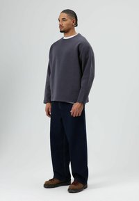 Grijze oversized sweatshirt met een ronde hals, gecombineerd met donkerblauwe loszittende spijkerbroek en bruine wandelschoenen. Subtiele textuur in de stof.