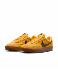 Sneaker gialli in suede con logo Nike swoosh nero, design a profilo basso, parte superiore testurizzata e suola in gomma marrone. Anche i lacci sono gialli.
