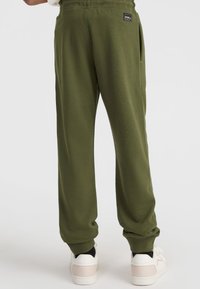 Grüne Jogginghose mit einem elastischen Bund, seitlichen Taschen und eng anliegenden Bündchen, kombiniert mit weißen Sneakers mit pinken Akzenten.