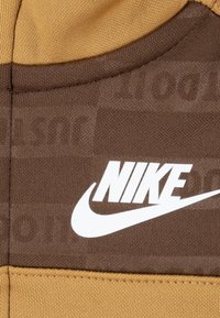 Rjava in svetlo rjava Nike tkanina z teksturiranim dizajnom; vsebuje izrazit bel Nike logotip. Vidne šive ob robovih.