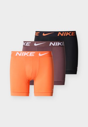 Három Nike férfi boxeralsó narancssárga, sötétlila és fekete színekben, márkajelzéssel ellátott derékpántokkal és Nike logókkal.