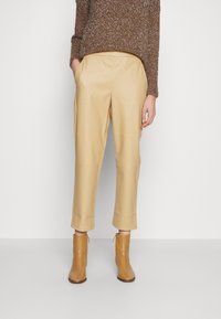 Beiga skräddarsydda byxor med synliga sidofickor och en slät yta, tillsammans med blanka tanfärgade ankelstövlar med blixtlås på sidan.