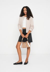 Gaiši beiga kardigāns, balts cropped tops, melnas denim svārkas ar saplēstu malu, melni dzīvokļi un daudzkrāsaina rokassoma ar pītas rokturīm.