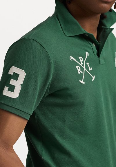 Grønn polo skjorte laget av teksturert stoff, har en hvit brodert nummer "3" på ermet og krossede polo-maler på brystet.