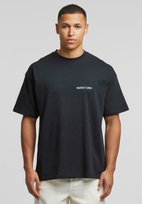 Tricou din bumbac negru, cu mâneci scurte și o croială lejeră. Are un mic logo albastru "AnotherCotton" pe partea stângă a pieptului. Design simplu.