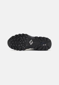 Black sneaker outsole with textured rubber, deep treads, and raised patterns. Features a visible logo and a 'AIR' accent on the side.