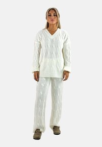 Maglione bianco a maglia cablè con scollatura a V e polsini a coste, abbinato a pantaloni larghi coordinati. Tessuto morbido, design accogliente.