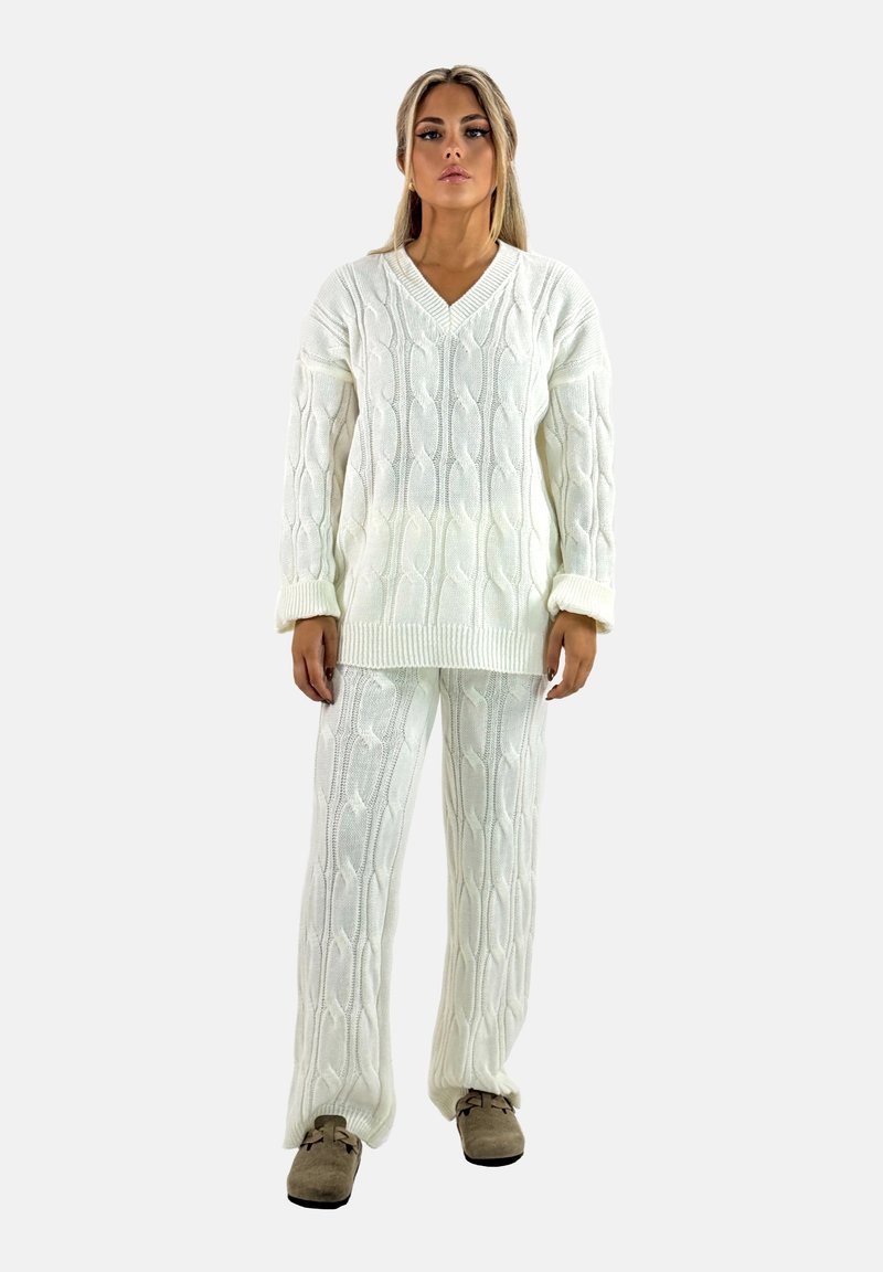 Maglione bianco a maglia cablè con scollatura a V e polsini a coste, abbinato a pantaloni larghi coordinati. Tessuto morbido, design accogliente.