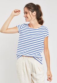 T-shirt en coton bleu et blanc à rayures, avec un col rond et des manches courtes, associé à un pantalon plissé beige clair.