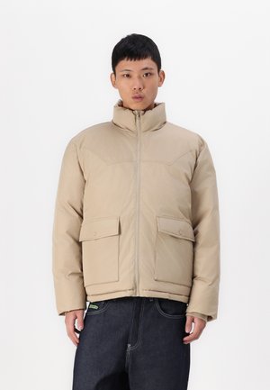 Beige puffer jacket with a high collar, front zipper, and two chest pockets. Features a smooth texture and minimalist design.