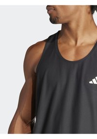 Primo piano di un uomo che indossa una maglietta atletica senza maniche nera con un logo bianco, che mostra la spalla, il collo e parte del volto girato di lato.
